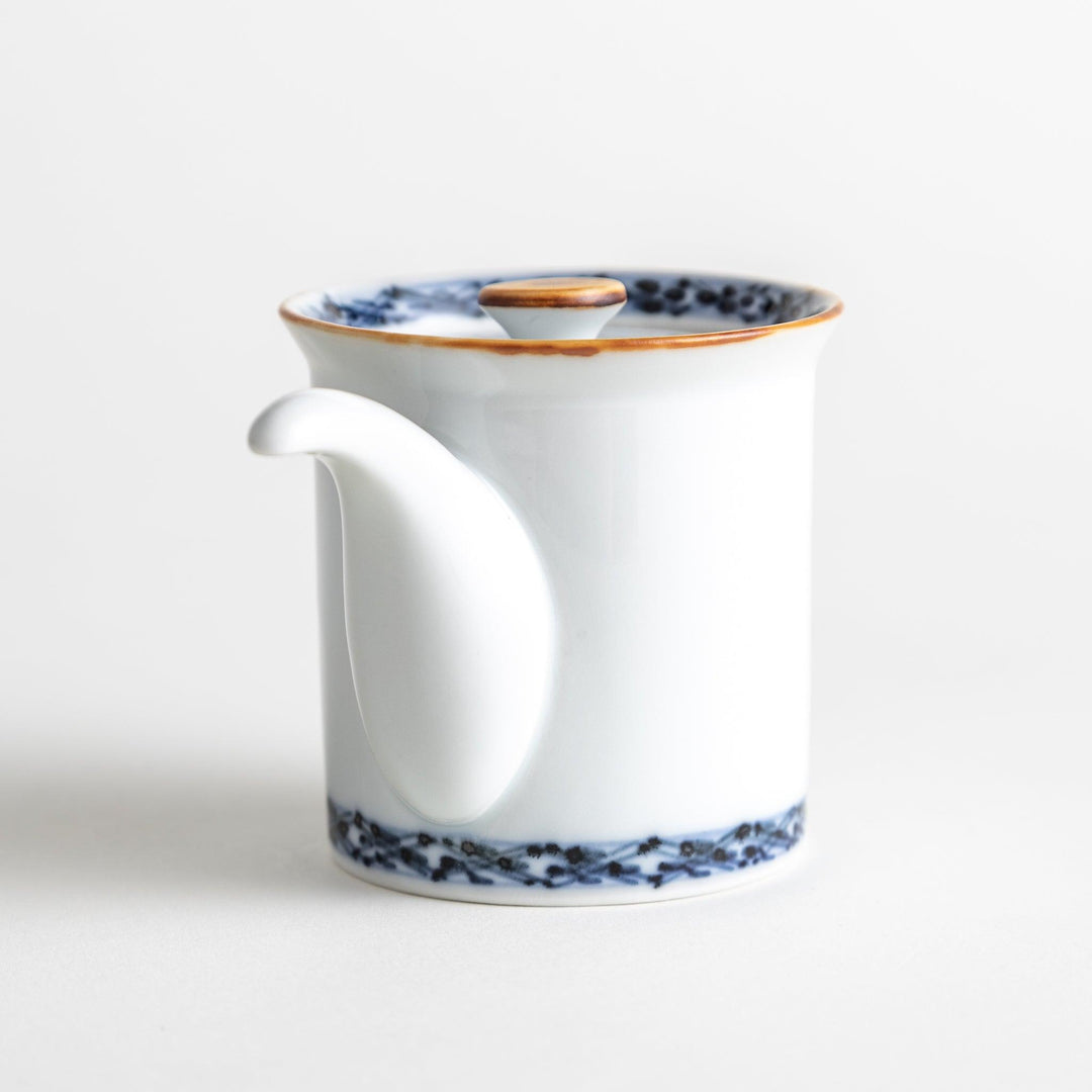 A small white ceramic soy sauce dispenser with a blue floral pattern along the rim.