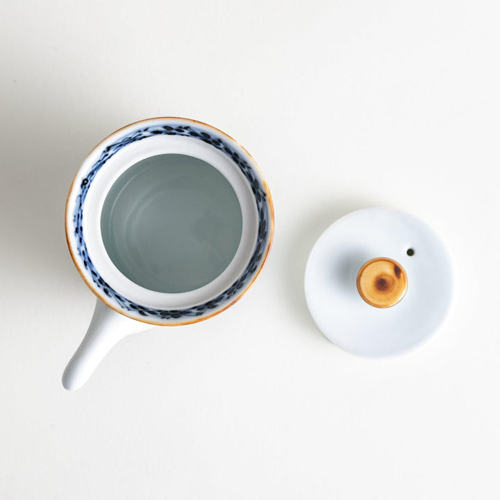 A small white ceramic soy sauce dispenser with a blue floral pattern along the rim.