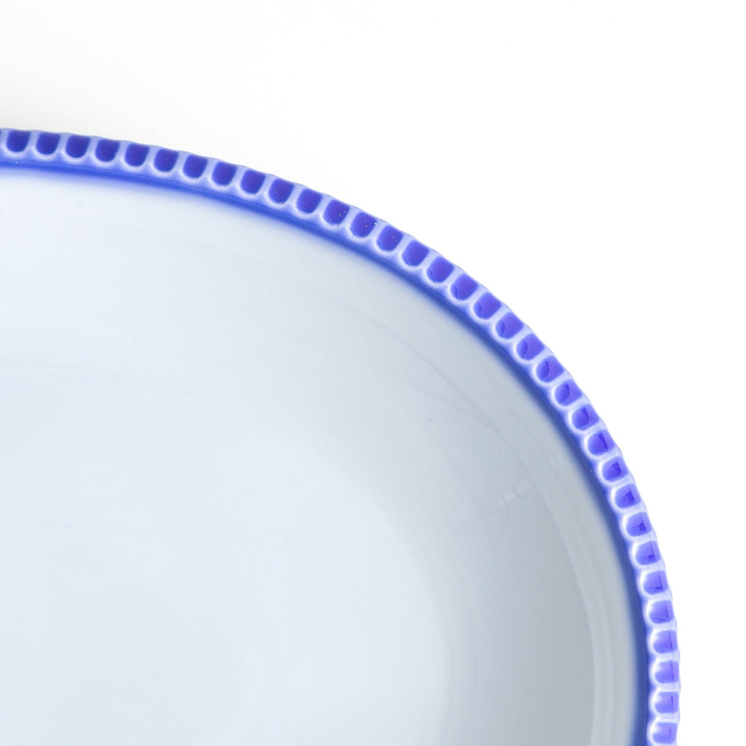 An oval-shaped white dinner plate with a rustic scallop-edged design. The border comes in blue, brown, and olive.