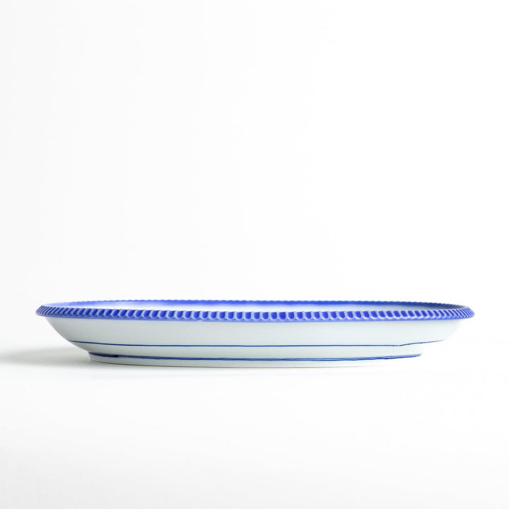 An oval-shaped white dinner plate with a rustic scallop-edged design. The border comes in blue, brown, and olive.