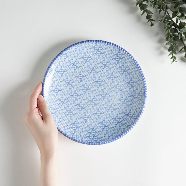 A round ceramic plate with a delicate blue floral pattern, accented by a textured blue rim.