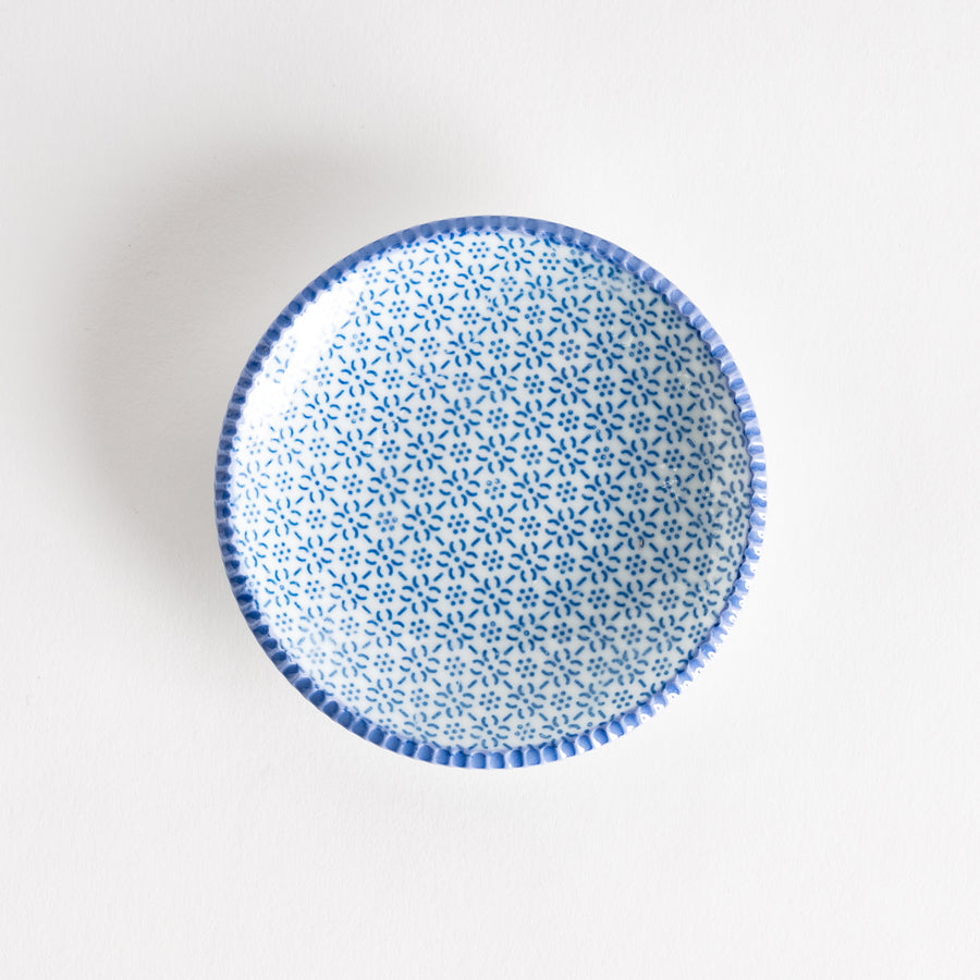 A round ceramic plate with a delicate blue floral pattern, bordered by a textured rim.