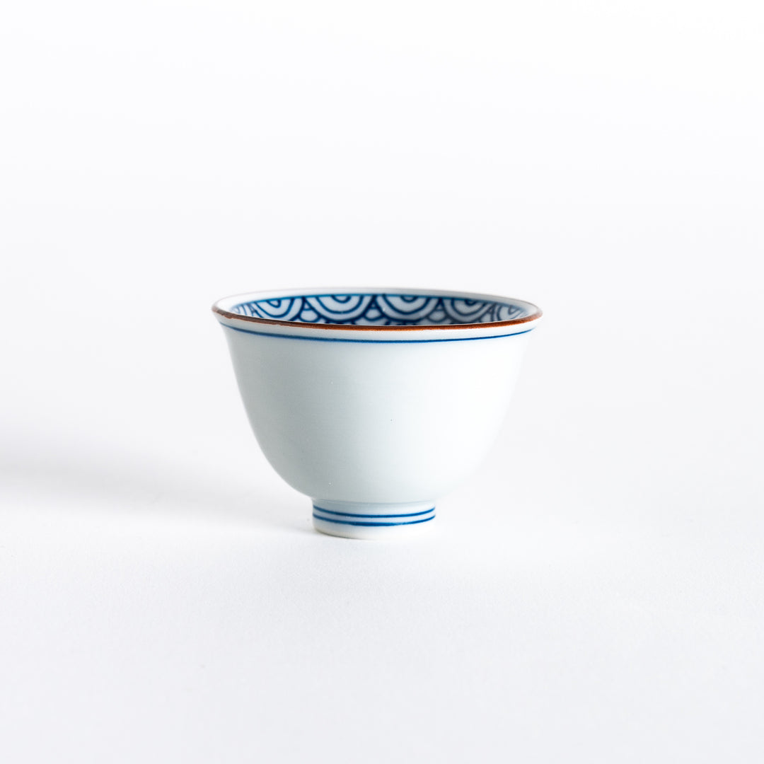 Front view of a white porcelain sake cup with blue wave patterns lining the inside rim and a gold accent.