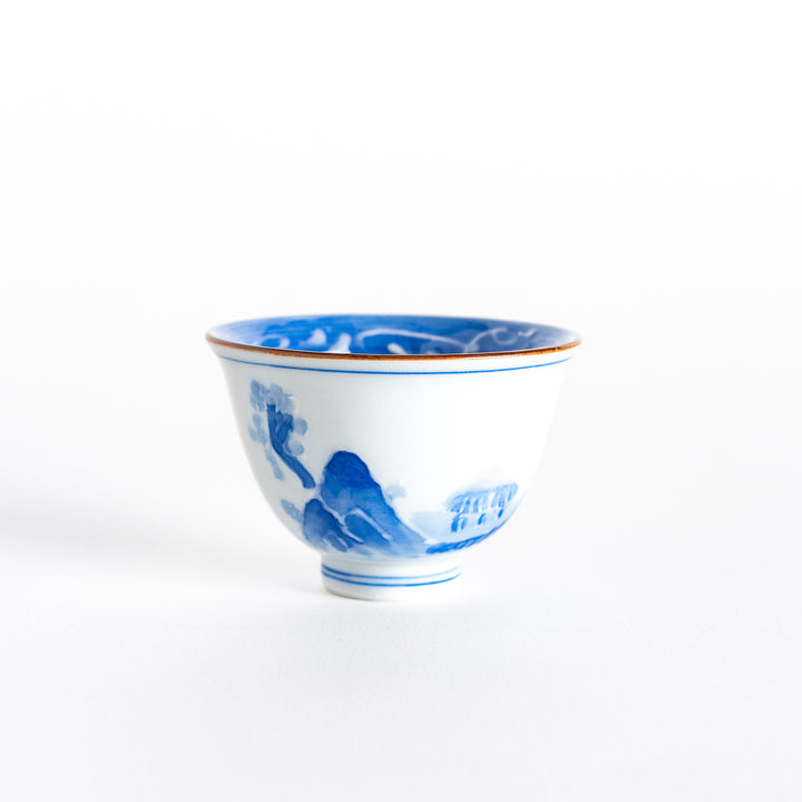 Front view of a blue and white porcelain sake cup featuring a hand-painted mountain and tree motif.