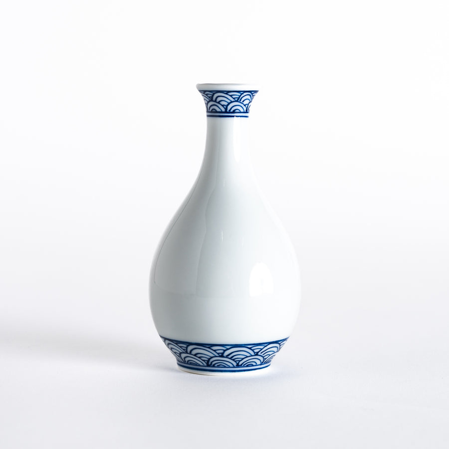 Front view of a white porcelain sake flask with a slender shape, adorned with blue wave patterns near the rim and base.