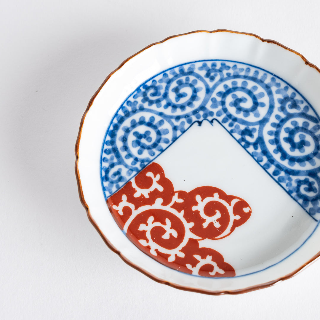 Close-up of a raised rim sauce dish with a blue arabesque pattern on top and red cloud motifs at the bottom, showing intricate detailing.