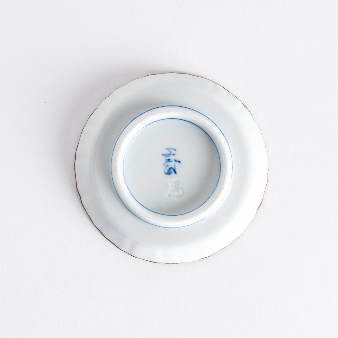 Bottom view of a raised rim sauce dish with blue arabesque patterns on top and red clouds at the bottom, with a maker's mark in blue.