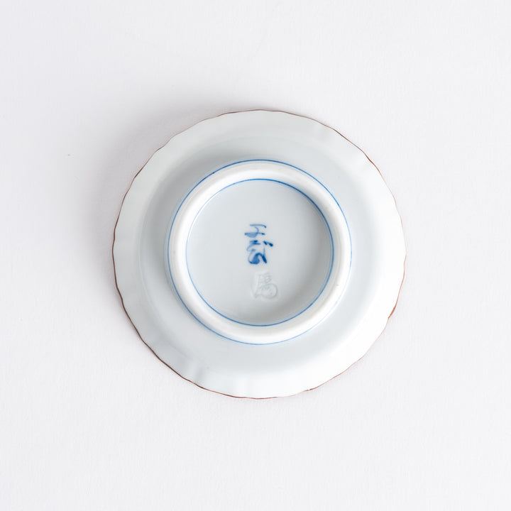 Bottom view of a raised rim sauce dish with blue arabesque patterns on top and red clouds at the bottom, with a maker's mark in blue.