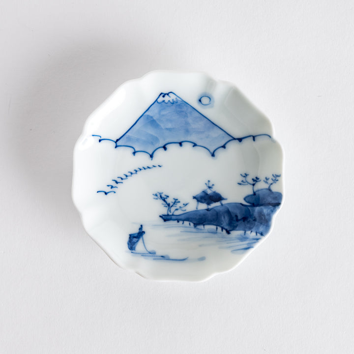 Blue and white rimmed sauce dish showcasing Mount Fuji and floral patterns against a light backdrop.