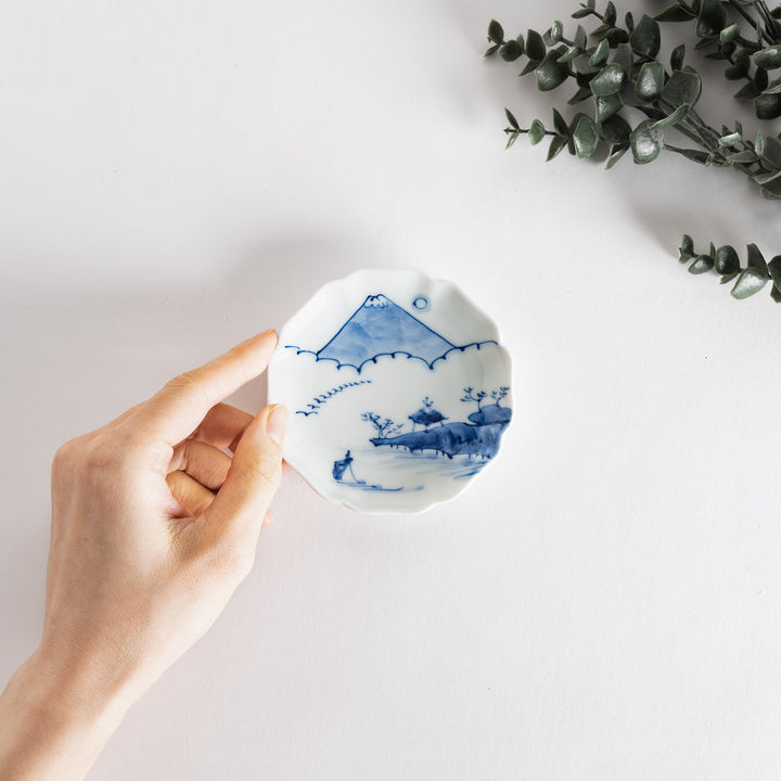 Hand holds a delicate blue and white sauce dish featuring scenic views of Mount Fuji and cherry blossoms.