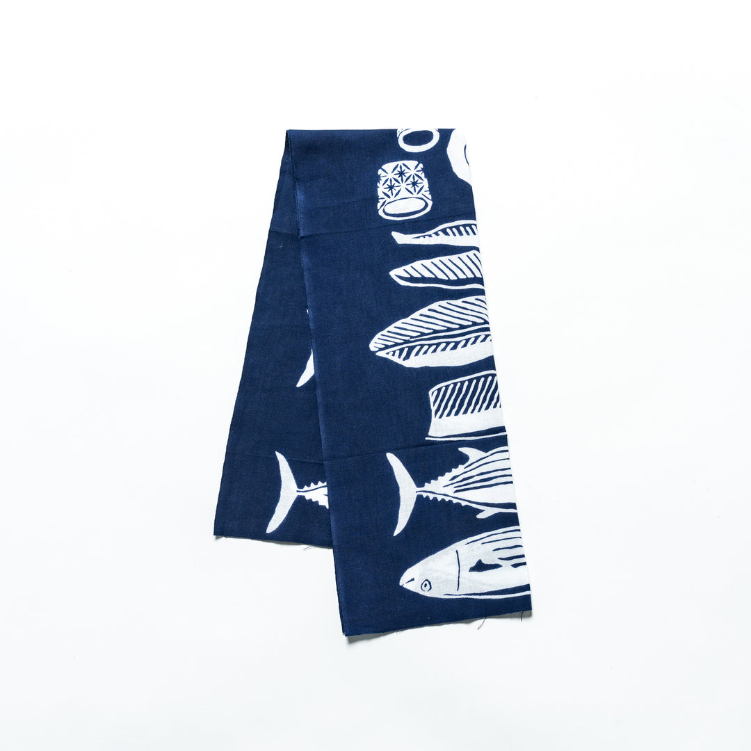 Navy blue tenugui hand towel featuring white fish and wave patterns, folded neatly.