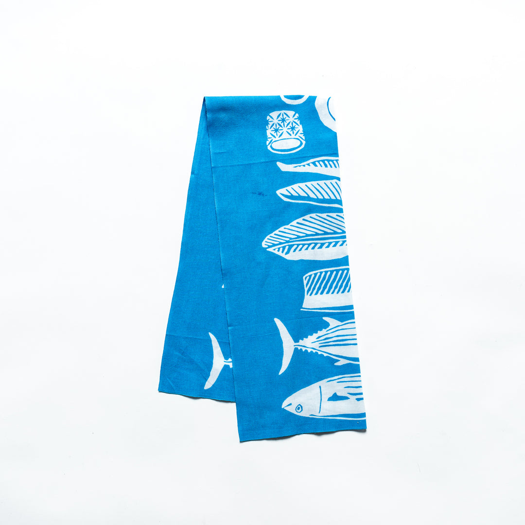 Light blue tenugui hand towel featuring white fish and wave patterns, folded neatly.