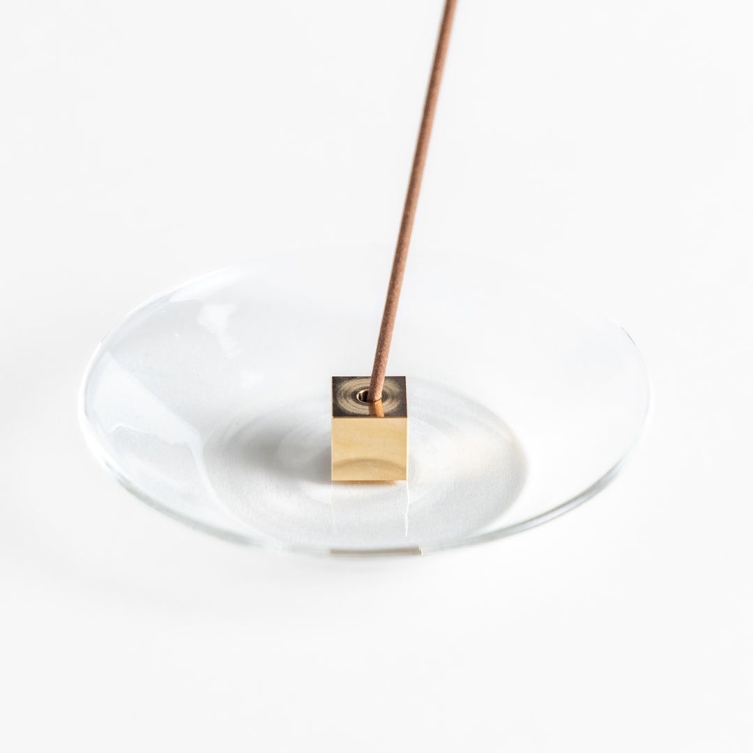 A modern Incense Holder set featuring a transparent glass dish and a brass cube stand, combining minimalist aesthetics with functionality for a refined incense experience.