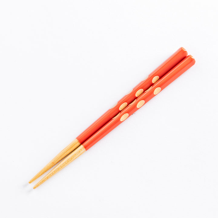 Red children's chopsticks with beige dots, placed on a white background, showing the tapered ends.