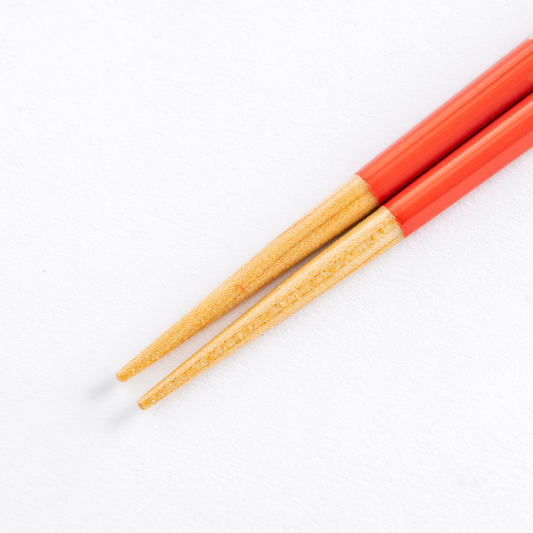 Close-up of red children's chopsticks with beige dots, highlighting the tips and wooden handles.