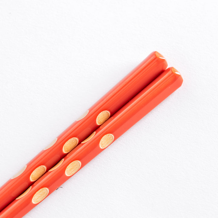 Close-up of red children's chopsticks, emphasizing the beige dots and textured surface near the tips.