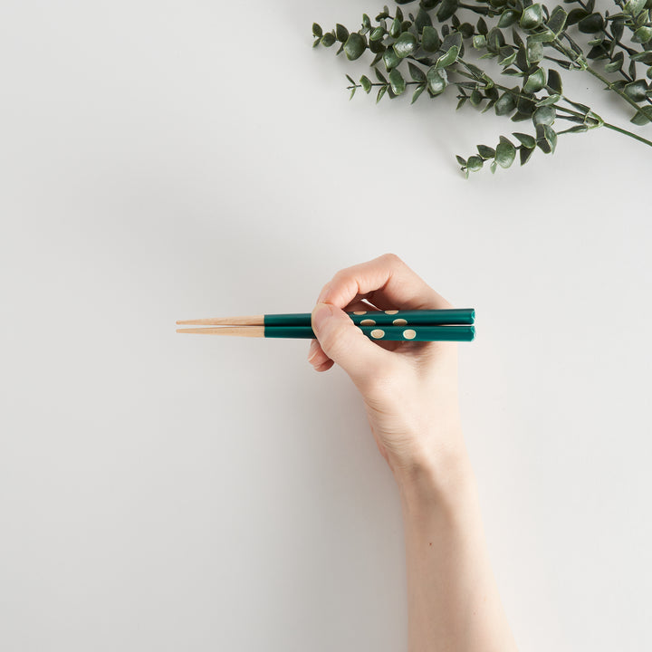 Green chopsticks held in hand, demonstrating size and comfortable grip for children.