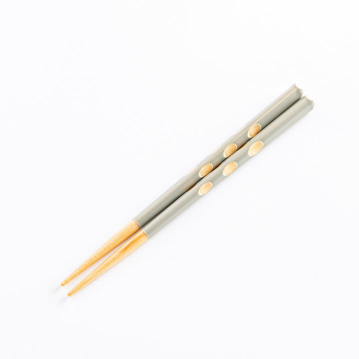 A pair of gray children's chopsticks with light wooden tips and decorative polka dots.