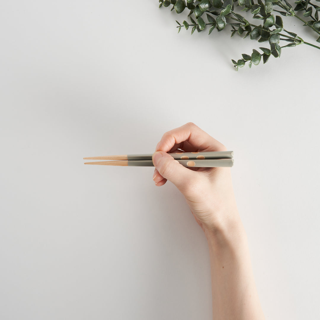 A hand holding gray chopsticks, demonstrating proper grip and featuring decorative polka dots.