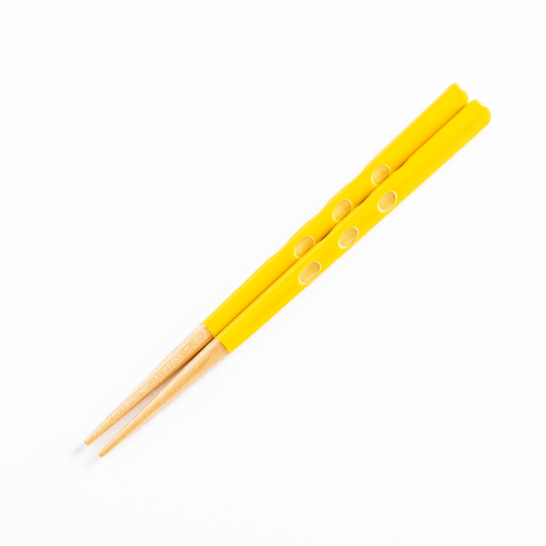 Yellow children's chopsticks displayed on a plain background, showcasing their polka dot pattern.