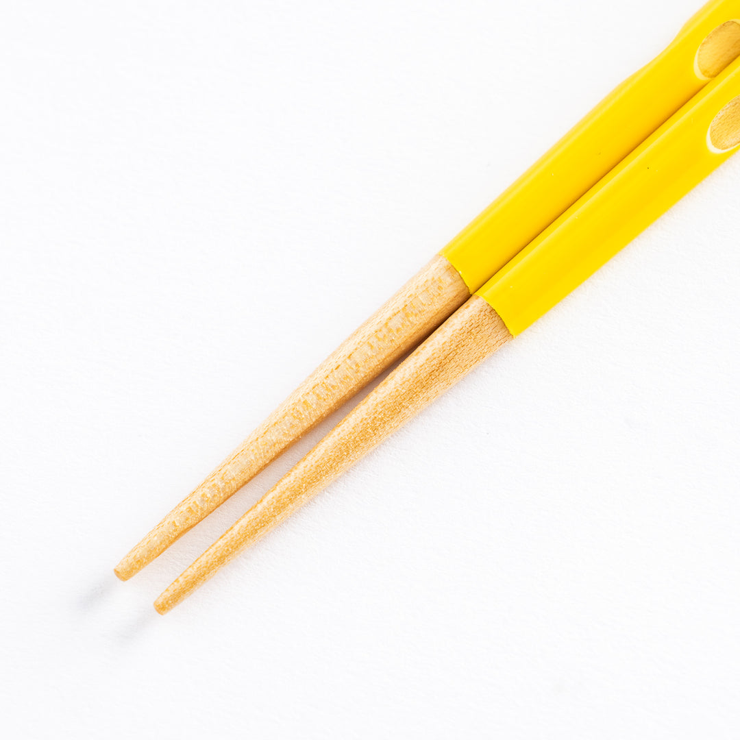 Close-up of the tips of the yellow children's chopsticks, highlighting the smooth finish and wooden ends.