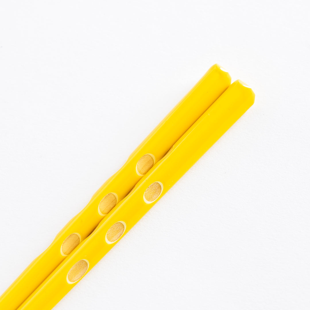 Close-up of the yellow children's chopsticks, emphasizing the polka dot design and rounded ends.