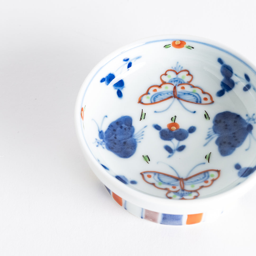 A petite raised sauce dish featuring colorful butterflies and floral designs, with multicolored vertical stripes along the base.