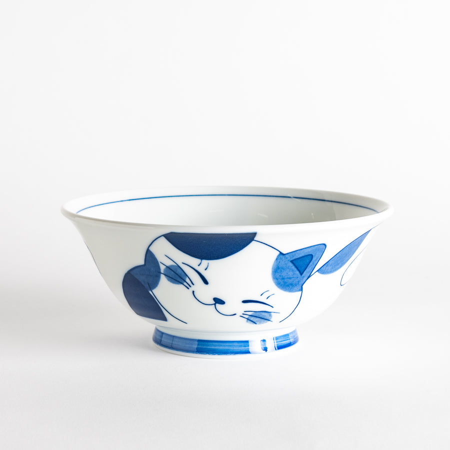 A white ramen bowl with a blue design of a cat with its ears back, looking relaxed.