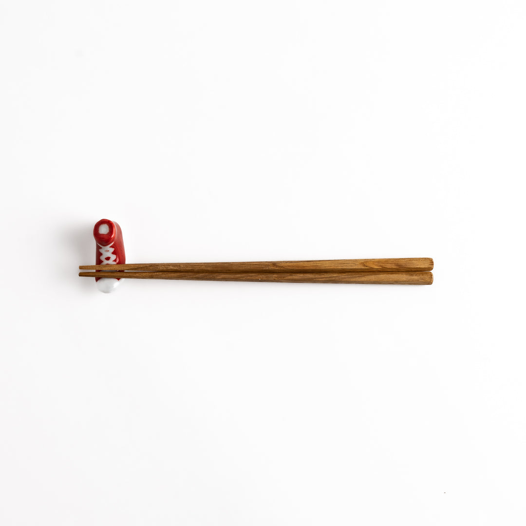 Red Canvas Sneaker Chopstick Rest holding wooden chopsticks, showcasing its vibrant design and practical functionality.