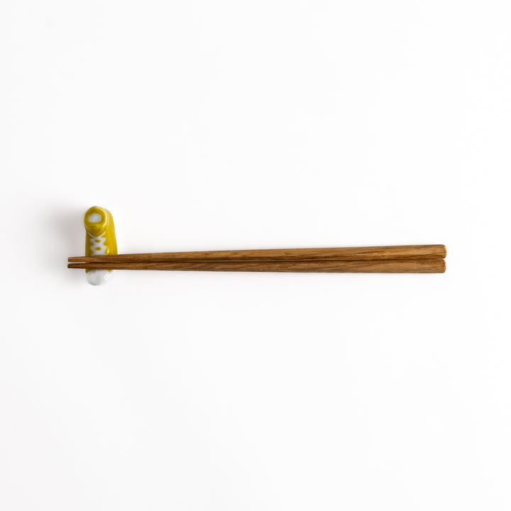 Yellow Canvas Sneaker Chopstick Rest holding wooden chopsticks, showcasing its vibrant design and practical functionality.