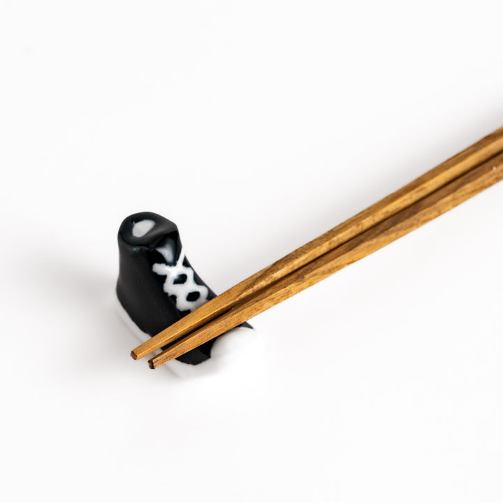 Black Canvas Sneaker Chopstick Rest holding wooden chopsticks, showcasing its vibrant design and practical functionality.