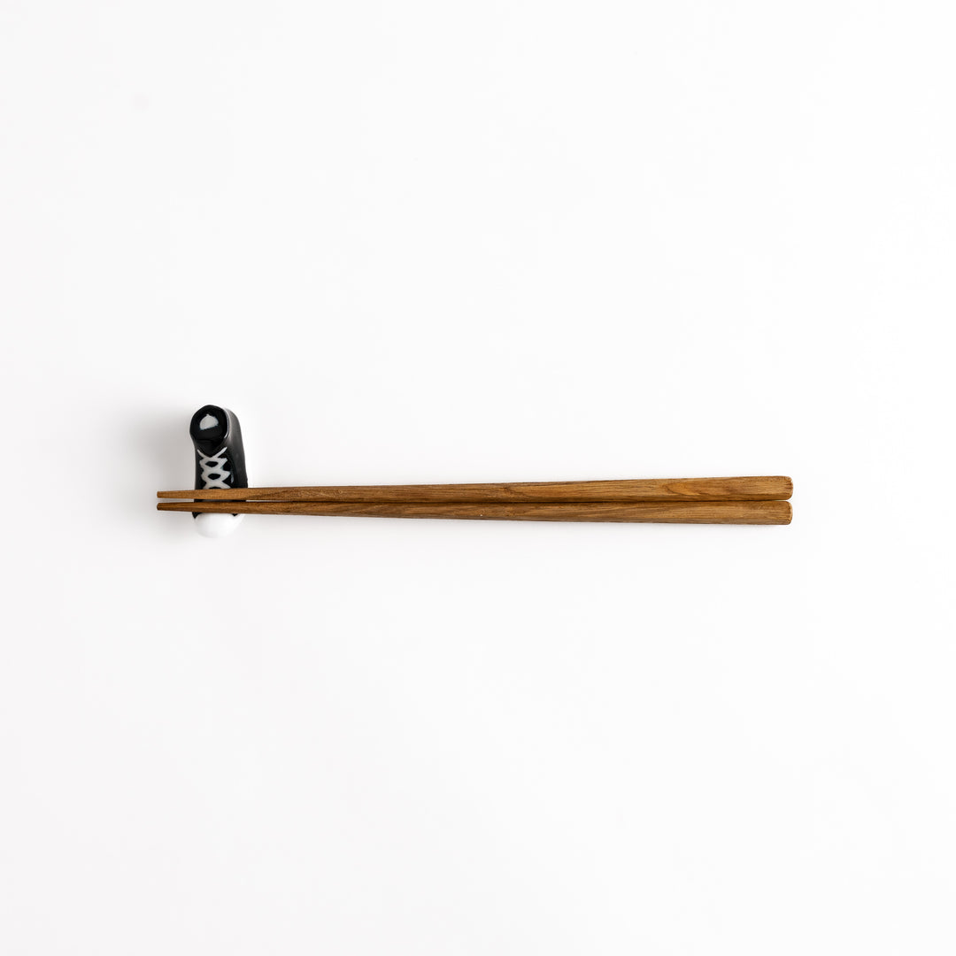 Black Canvas Sneaker Chopstick Rest holding wooden chopsticks, showcasing its vibrant design and practical functionality.