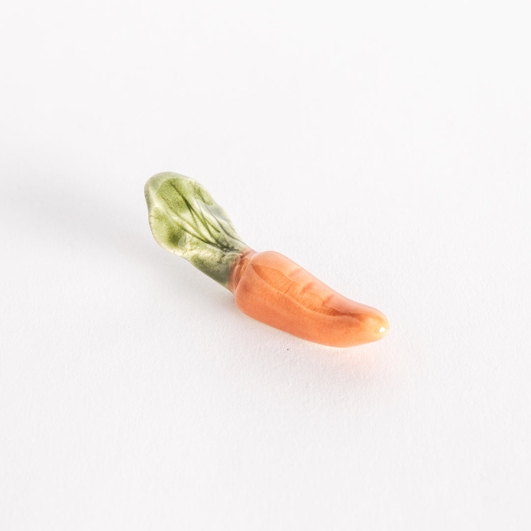 Angled view of ceramic carrot chopsticks rest, emphasizing its orange color and green leafy details.