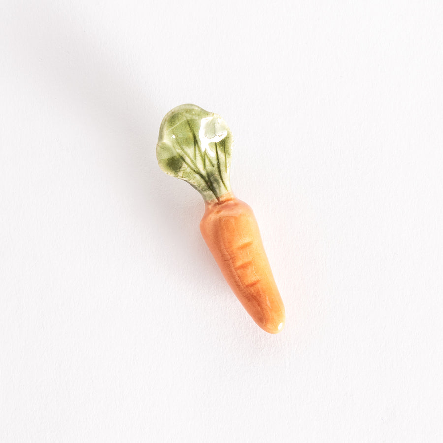 Bright orange carrot-shaped ceramic chopsticks rest with green leafy details on top.