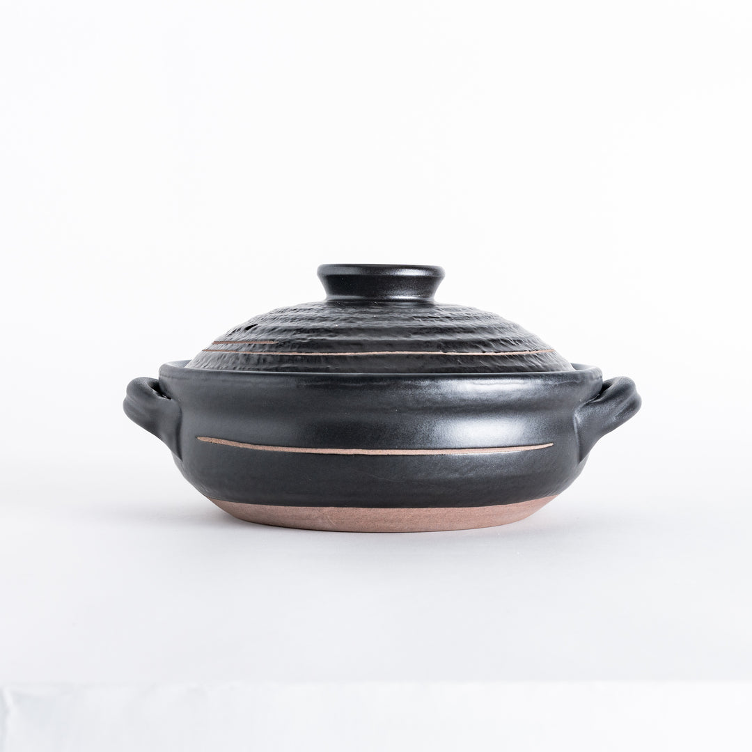 Side view of the black ceramic donabe, showing its round handles and subtle carved design.