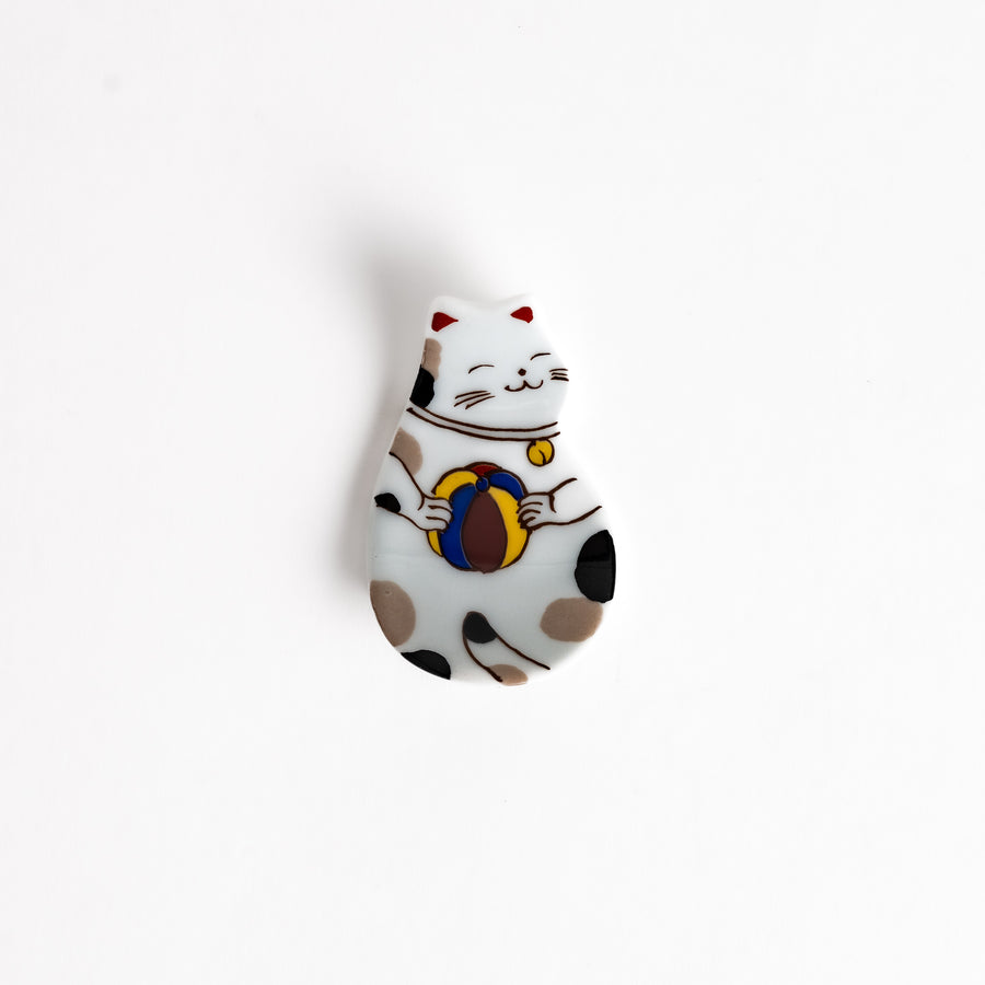 Ceramic chopsticks rest shaped like a cat holding a ball, featuring detailed brown, black, and red accents with a charming expression.