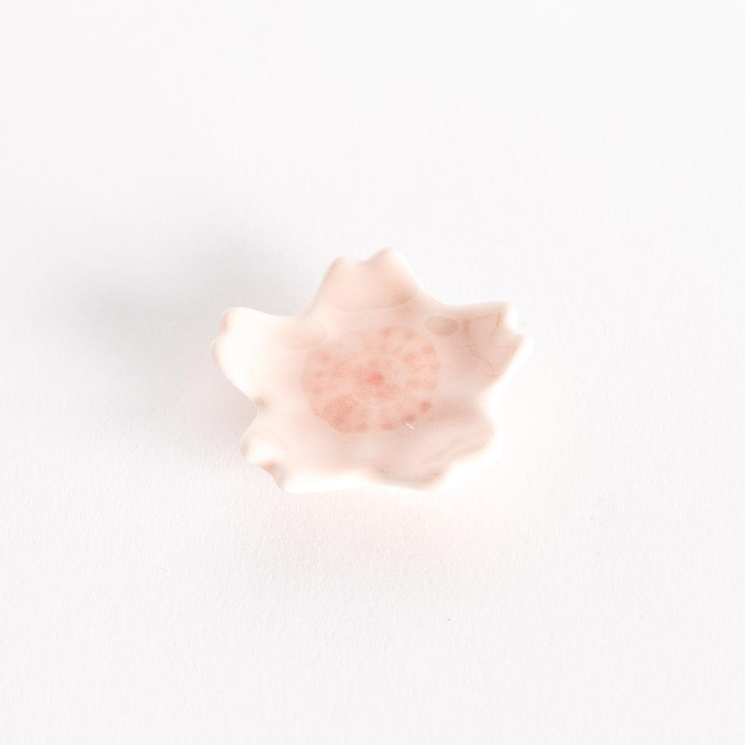 Pink cherry blossom-shaped chopstick rest photographed slightly angled, emphasizing its delicate petal design.