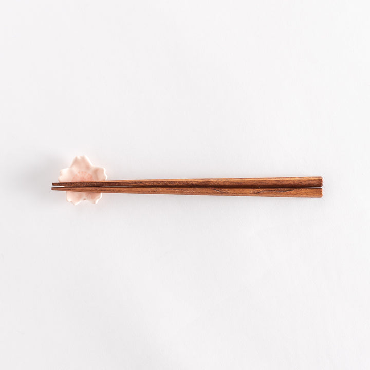 Pink cherry blossom chopstick rest holding a pair of chopsticks, showcasing its soft pastel finish and detailed center.