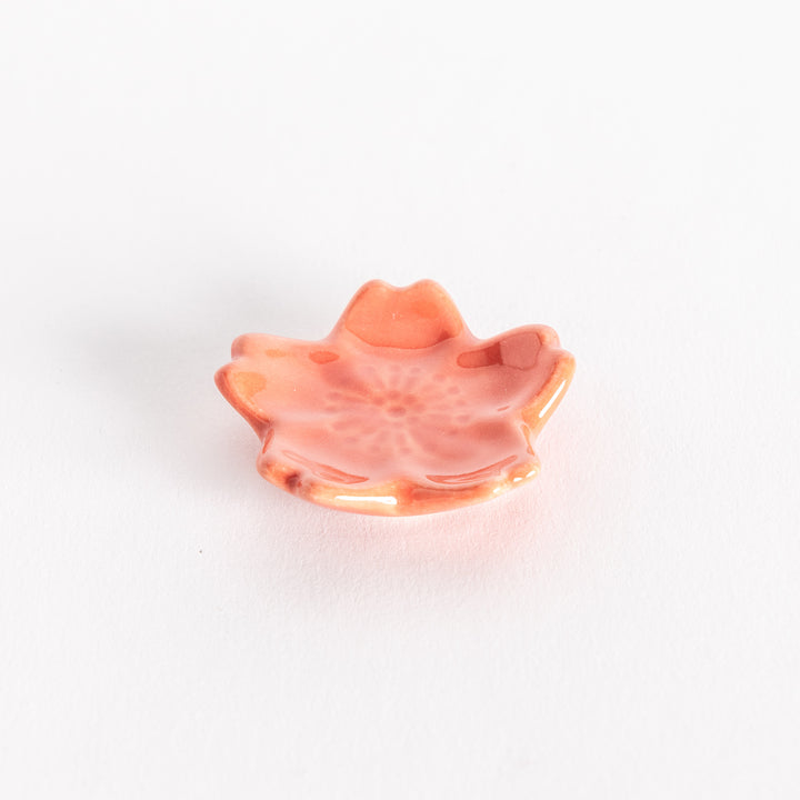 Vermilion cherry blossom-shaped chopstick rest photographed at an angle, showing its petal curves and details.