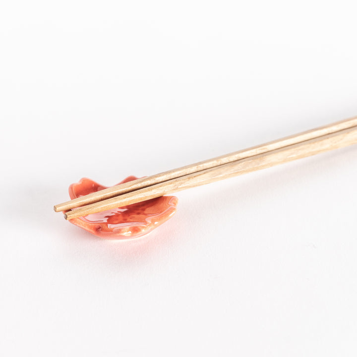 Close-up of a vermilion cherry blossom chopstick rest with chopsticks resting gently across its glossy surface.