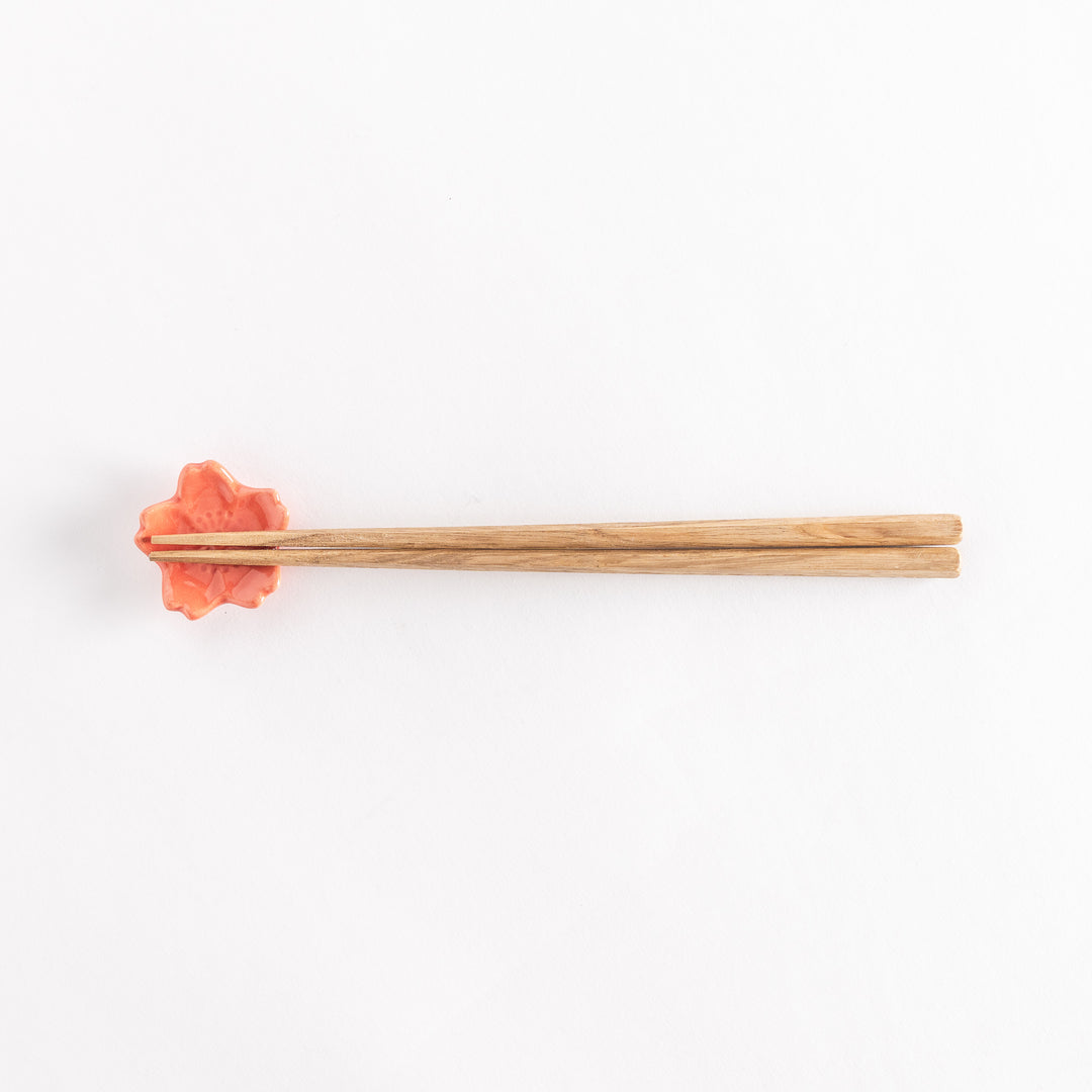 Vermilion cherry blossom chopstick rest holding chopsticks, highlighting its glossy finish and floral design.