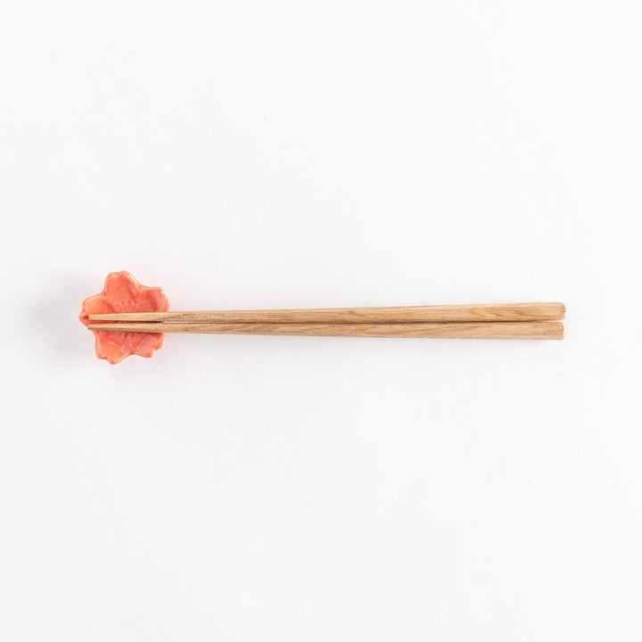 Vermilion cherry blossom chopstick rest holding chopsticks, highlighting its glossy finish and floral design.