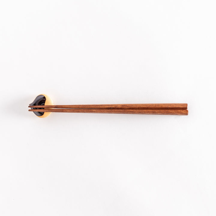 The chestnut chopsticks rest with chopsticks resting across it, emphasizing its curved shape.