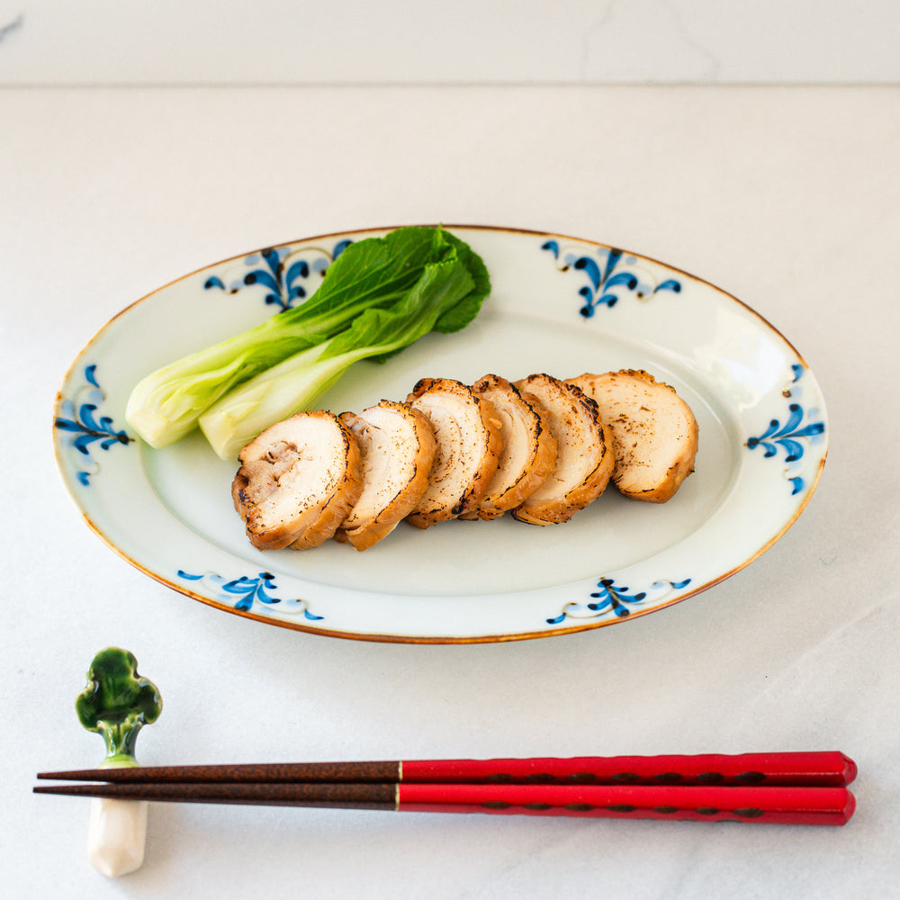 Top view of sliced chicken chashu, served with a side of bok choy, placed on an oval plate with blue floral patterns.