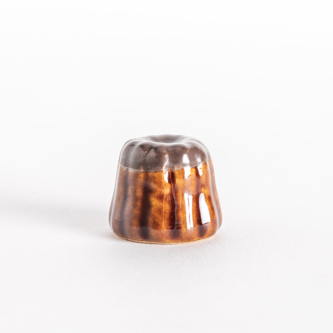 A front-facing view of the ceramic chocolate canelé chopstick rest, highlighting its curved ridges and smooth top.