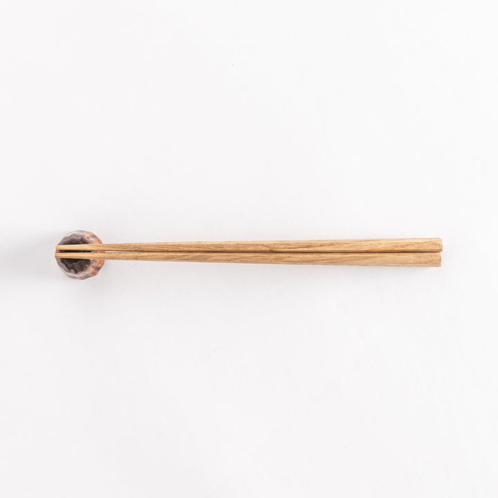 A wide view of the chocolate canelé chopstick rest with chopsticks placed on it, emphasizing its charming and unique design.