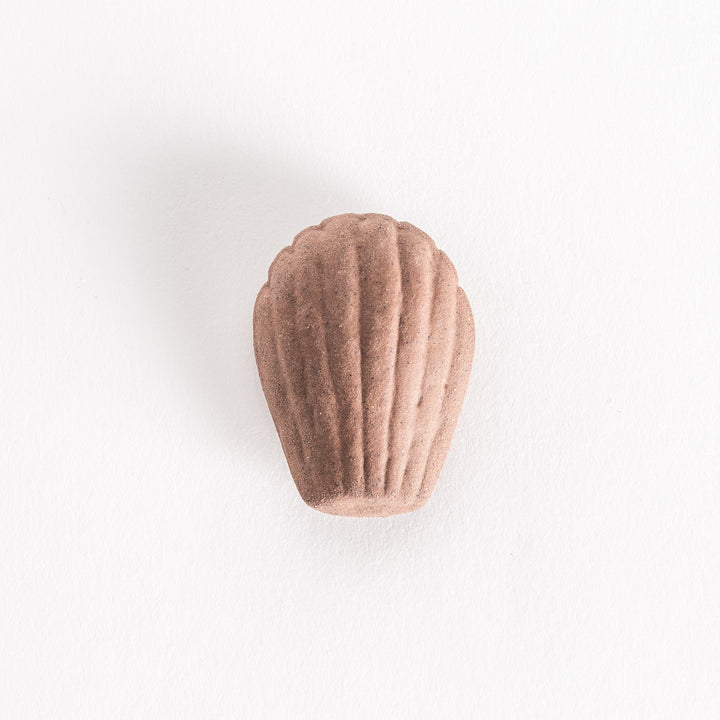 A ceramic chopstick rest shaped like a chocolate madeleine, featuring a textured brown surface, placed on a white background.