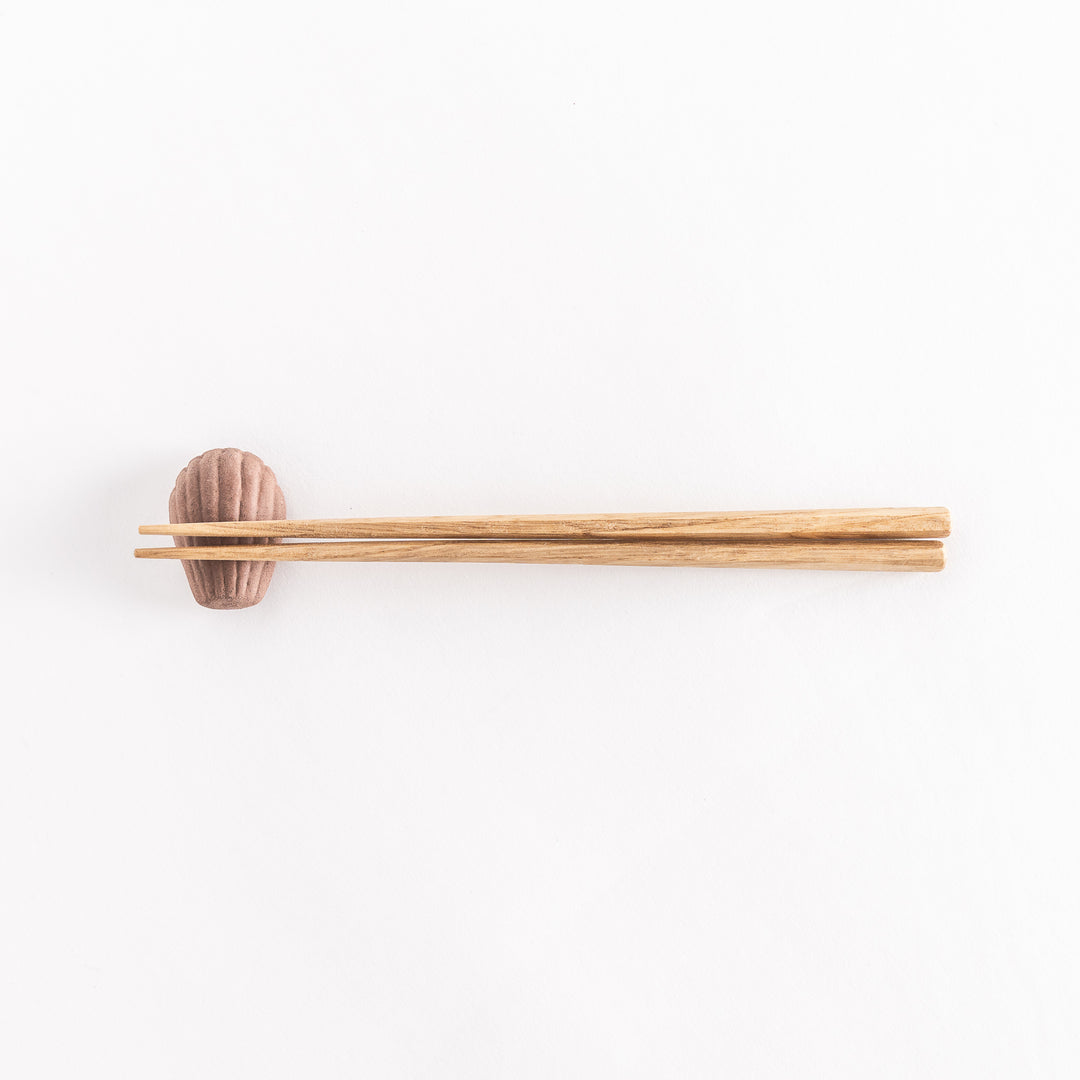 A wide view of the ceramic chocolate madeleine chopstick rest with chopsticks resting on it, emphasizing its elegant shape.