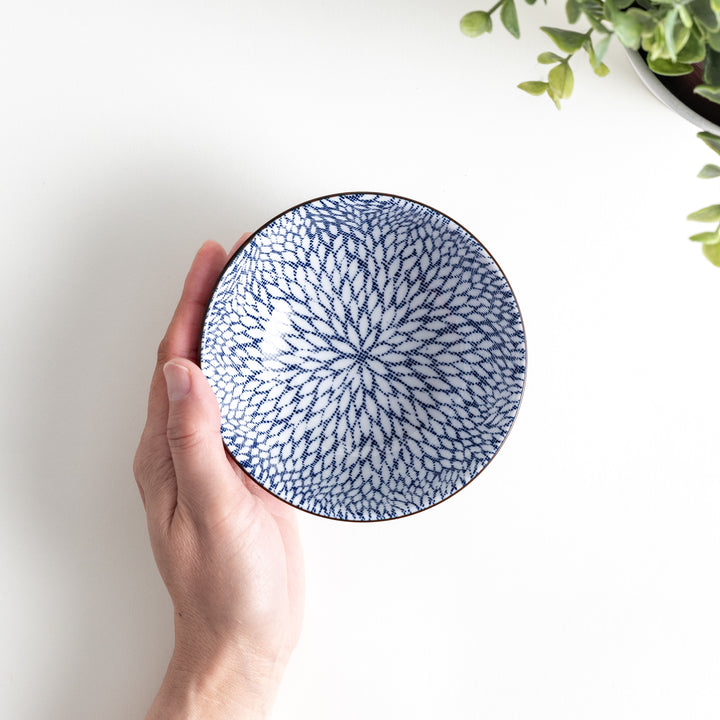 Person holding the bowl, showing the top view of the intricate blue design against a light background.