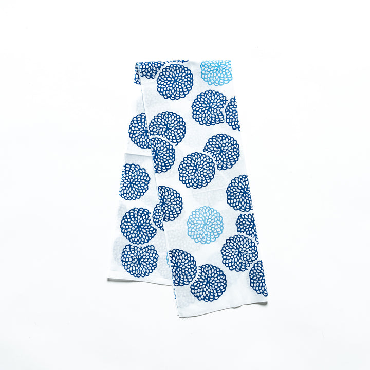 Blue chrysanthemum-patterned tenugui hand towel with white accents, neatly folded.